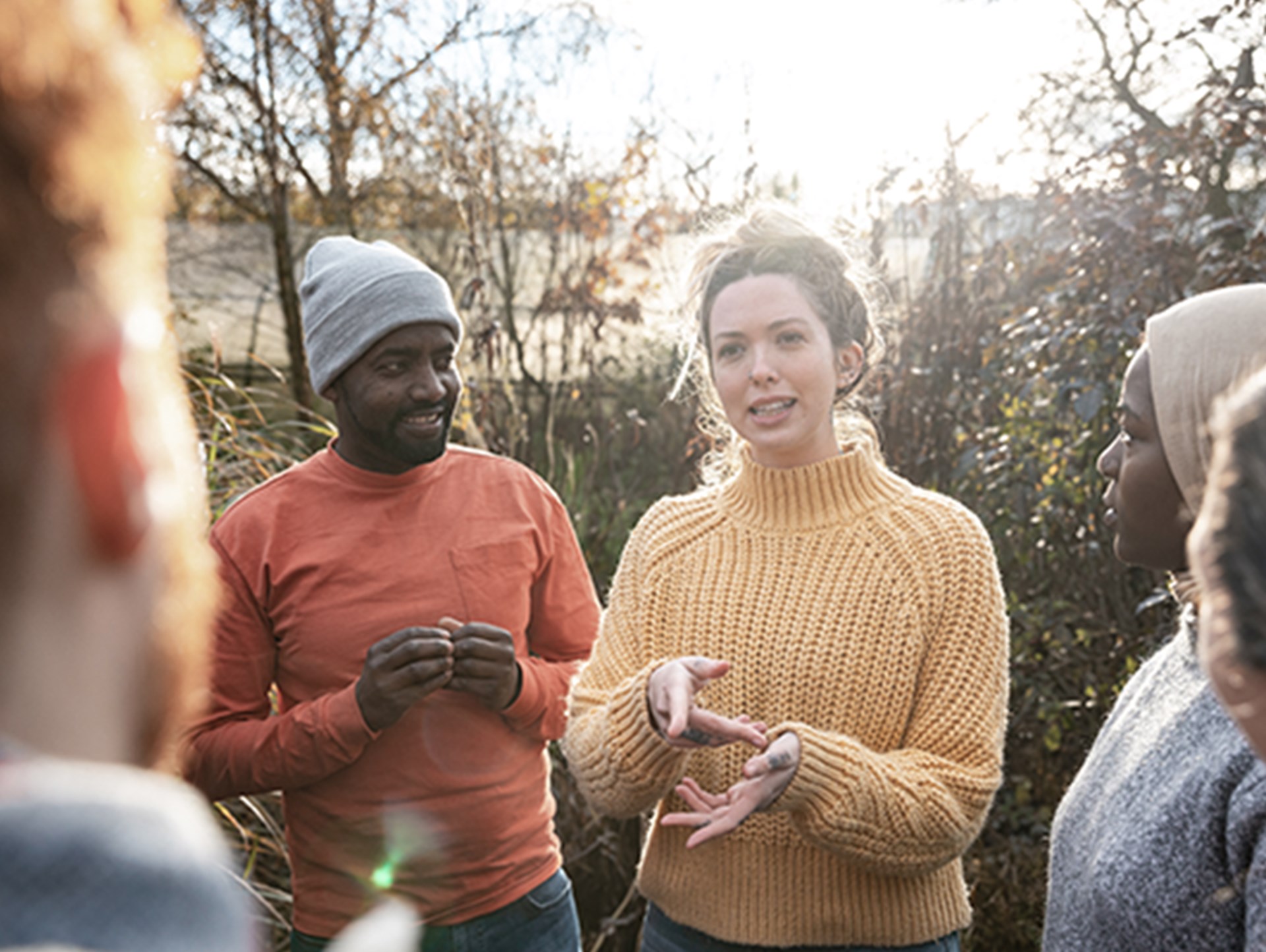 Eine Gruppe von Freiwilligen, die an einem sonnigen, kalten Wintertag in warmer Freizeitkleidung im Garten steht. Die junge Frau in der Mitte des Bildes erklärt etwas. 