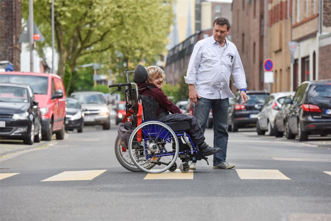 Betreuer und Mann mit Behinderung im Rollstuhl auf der Straße