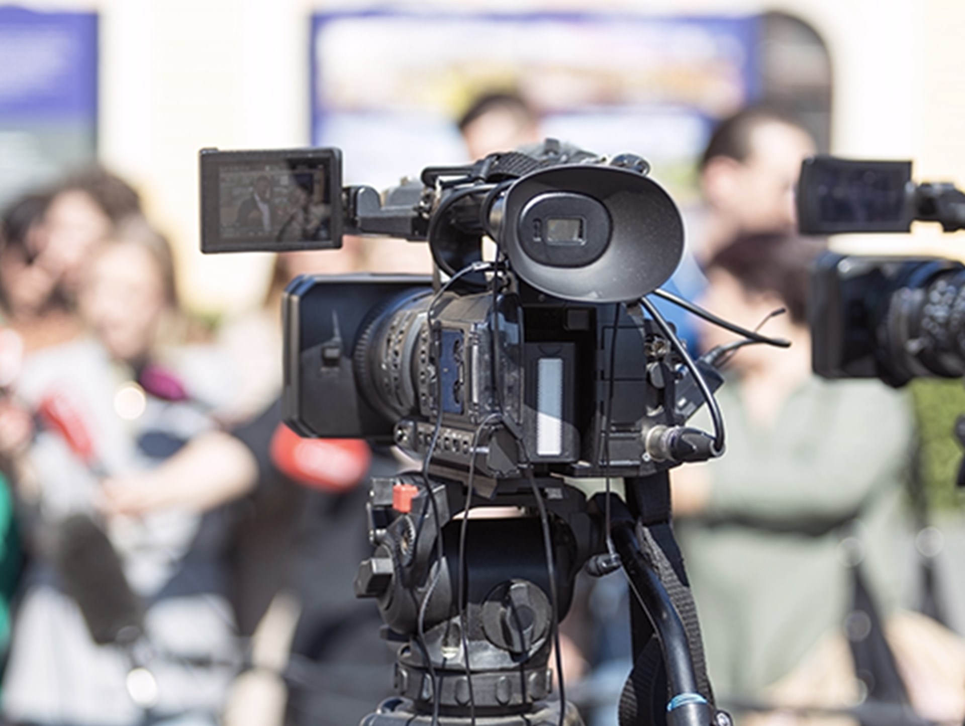 Professionelle Videokameras, die so eingerichtet sind, dass sie eine Live-Pressekonferenz aufzeichnen, während sich Reporter und Teilnehmer im Hintergrund versammeln.