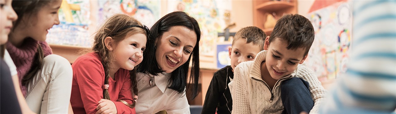 Eine Erzieherin zeigt Kindern, die viel Spaß haben, etwas auf dem Boden