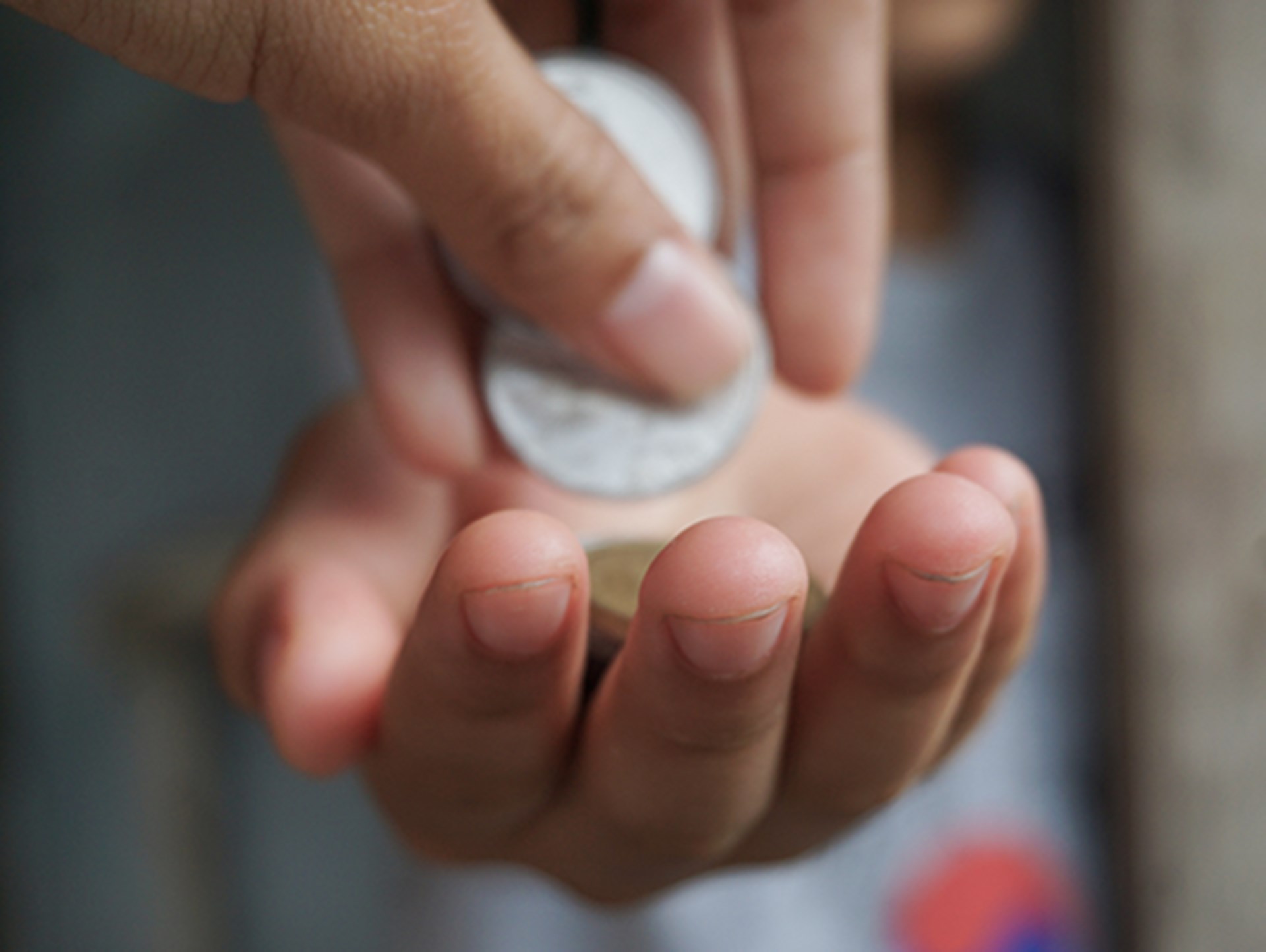 Es sind zwei Hände zu sehen. Die untere Hand ist geöffnet und zeigt mit der Handinnenseite nach oben. Die zweite Hand legt in die geöffnete Hand Geldstücke. Dieses Stockfoto symbolisiert eine Geldspende. 