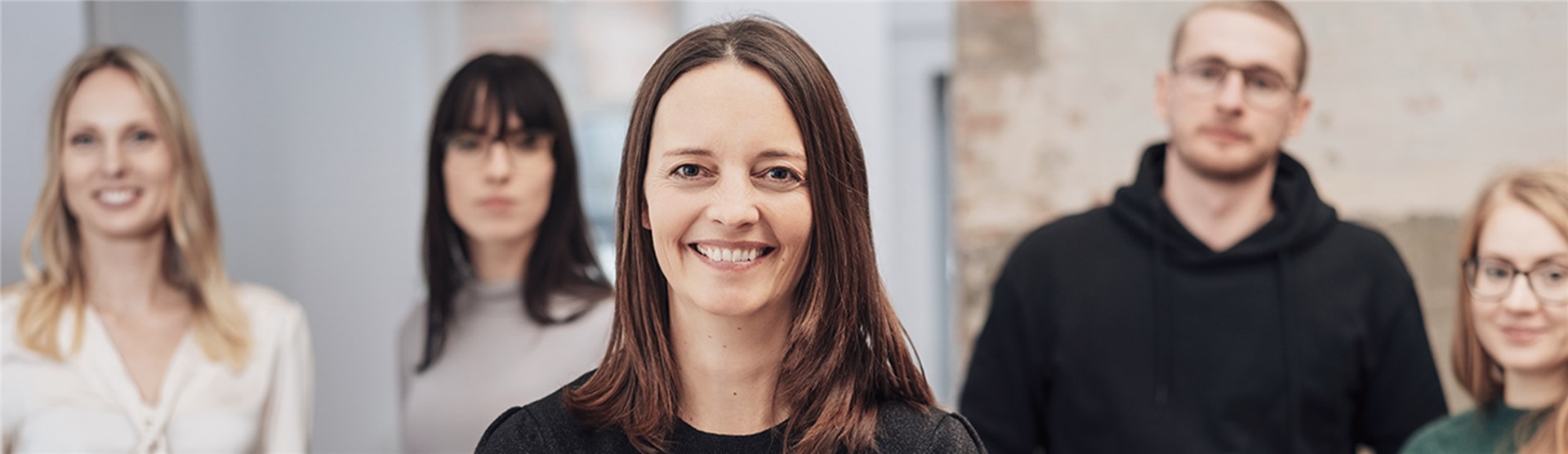 Eine Gruppe Menschen lächelt in die Kamera. Nur die Dame ganz vorne ist klar zu erkennen. Die drei Personen im Hintergrund sind unscharf.