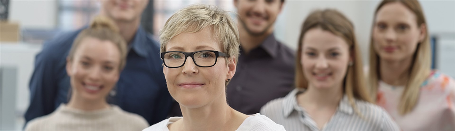 Eine Gruppe Menschen lächelt in die Kamera. Nur die Dame ganz vorne ist klar zu erkennen. Die fünf Personen im Hintergrund sind unscharf.