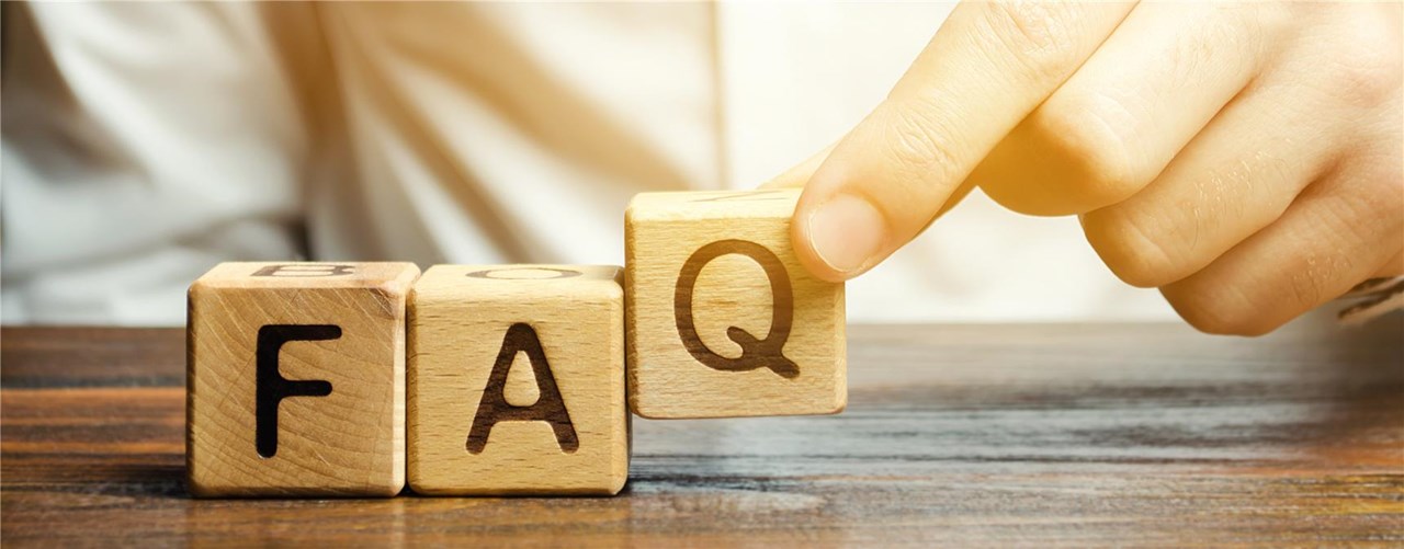 Eine Hand ist zu sehen, die Würfel mit den Buchstaben FAQ auf einen Tisch stellt.