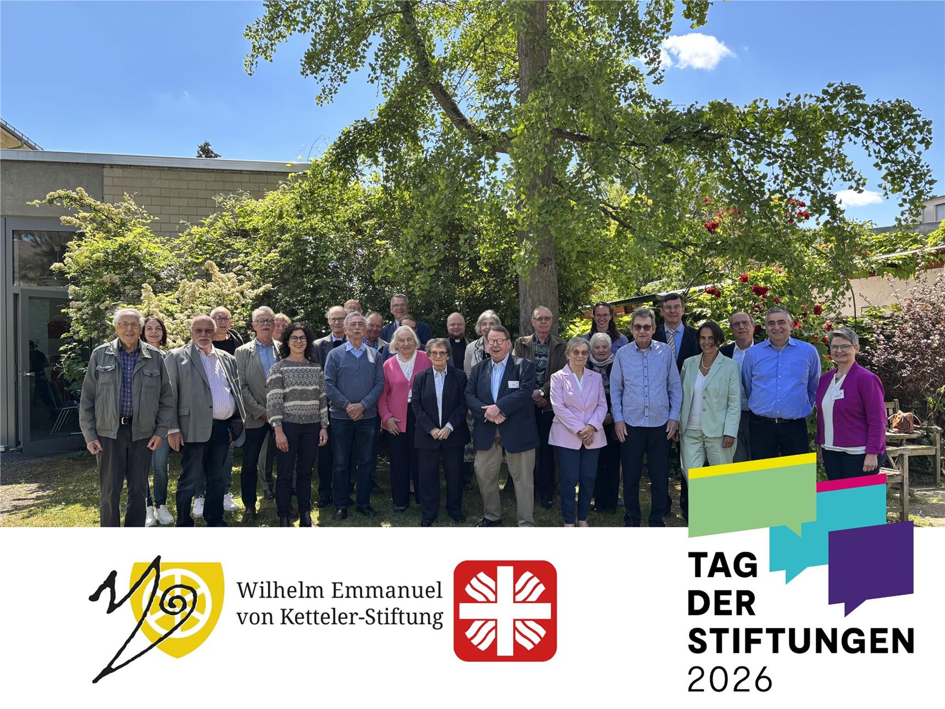 Rund 40 Menschen, darunter Stifterinnen und Stifter sowie Gremienmitglieder der Wilhelm Emmanuel von Ketteler-Stiftung, posieren für ein Gruppenbild bei blauem Himmel vor einem Baum.