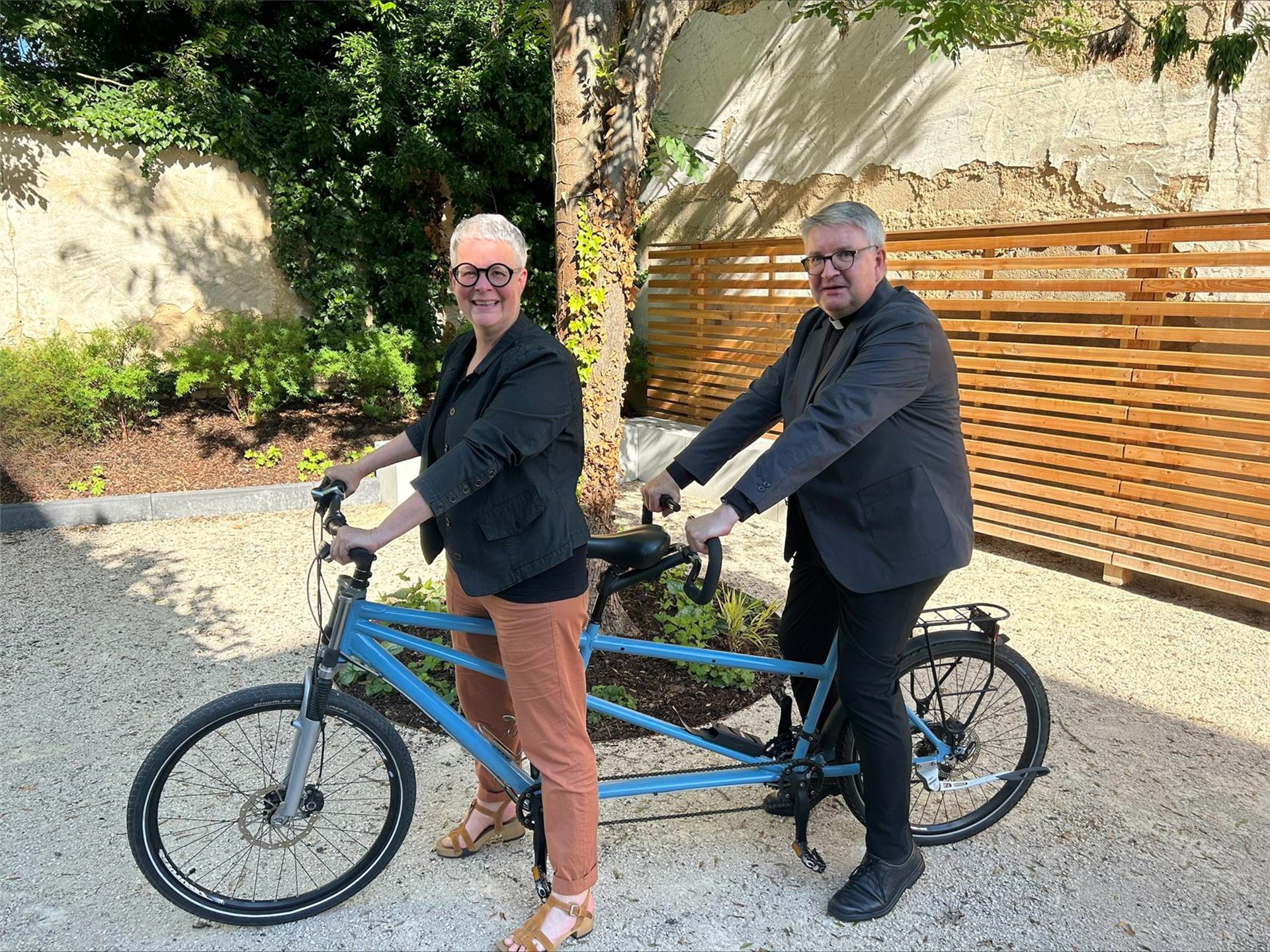 Zwei Personen sitzen zusammen auf einem blauen Tandem und lächeln in die Kamera.