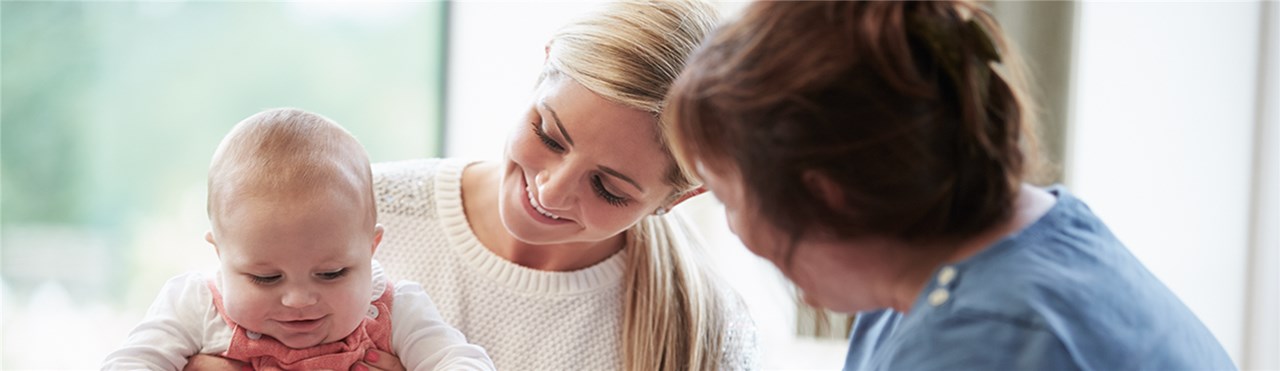 Frau die ihr Baby auf dem Schoß hält und von einer anderen Frau Untertsützung bekommt
