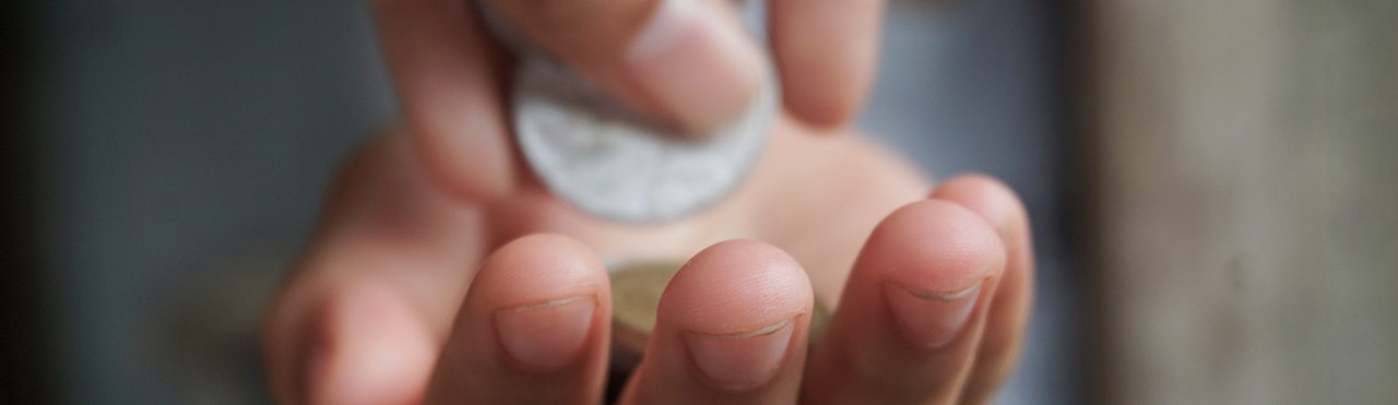 Es sind zwei Hände zu sehen. Die untere Hand ist geöffnet und zeigt mit der Handinnenseite nach oben. Die zweite Hand legt in die geöffnete Hand Geldstücke. Dieses Stockfoto symbolisiert eine Geldspende. 