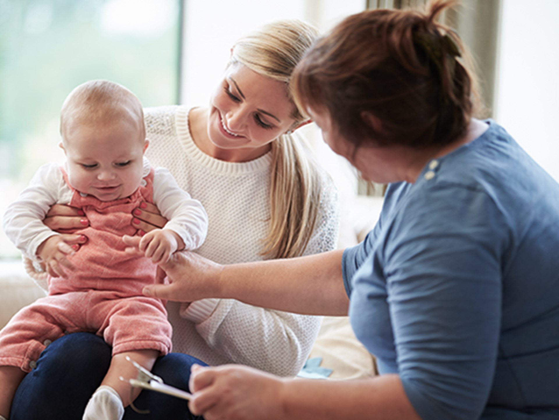 Frau die ihr Baby auf dem Schoß hält und von einer anderen Frau Untertsützung bekommt